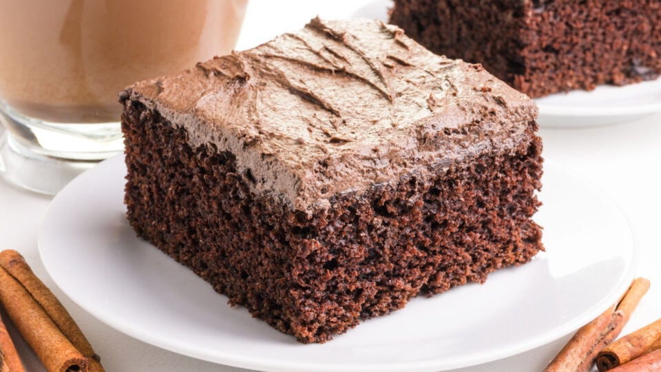 A slice of chai chocolate cake on a plate with cinnamon sticks beside it.