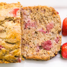 Looking down on a loaf of strawberry banana bread with one slice laying in front of it along with fresh strawberries.