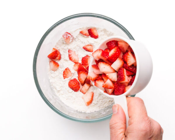 Chopped strawberries are being poured into a mixing bowl with a flour mixture.