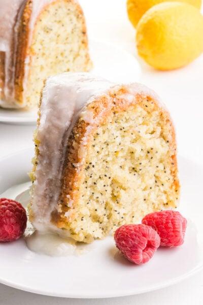 A slice of lemon poppyseed cake on a plate next to fresh raspberries.