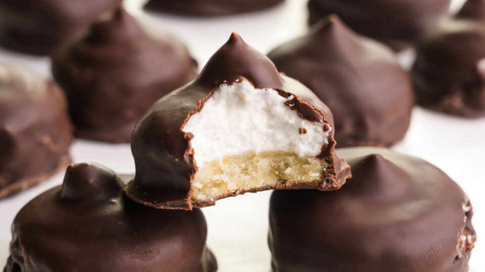 Vegan mallomars shows one with a bite taken out revealing marshmallow cream inside.
