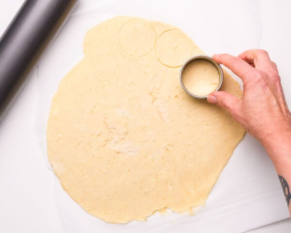 A hand uses a round cookie cutter to cut cookie dough into circles.