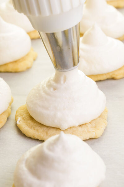 Marshmallow cream is being piped onto fop of baked cookies.