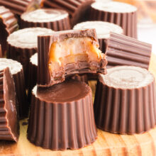 A vegan rolo has a bite taken out showing gooey caramel inside of a chocolate candy shell.