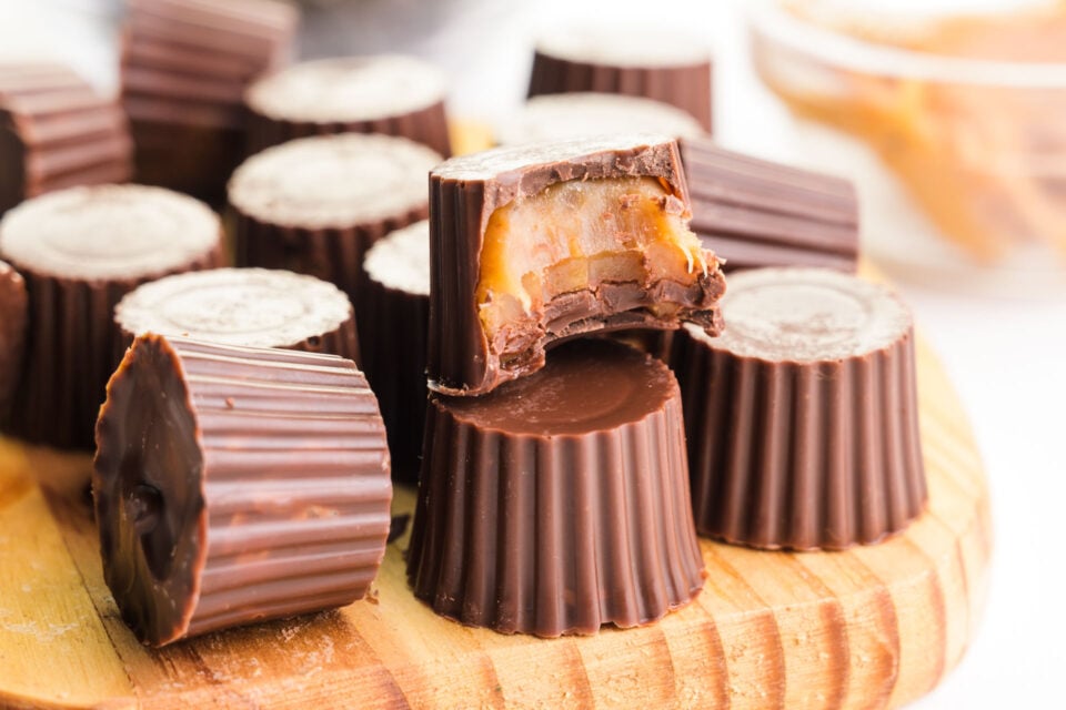 Several vegan chocolate candies are on a cutting board, one with a bite taken out revealing caramel inside of a chocolate shell.
