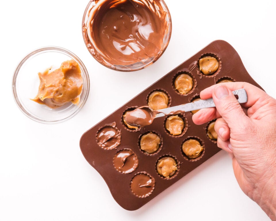 Melted chocolate is being drizzled into candy molds over caramel filling.