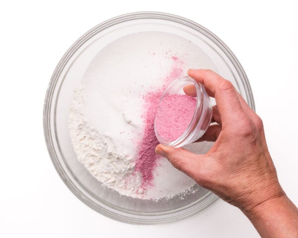 Strawberry jello mix is being poured into a mixing bowl with flour ingredients.