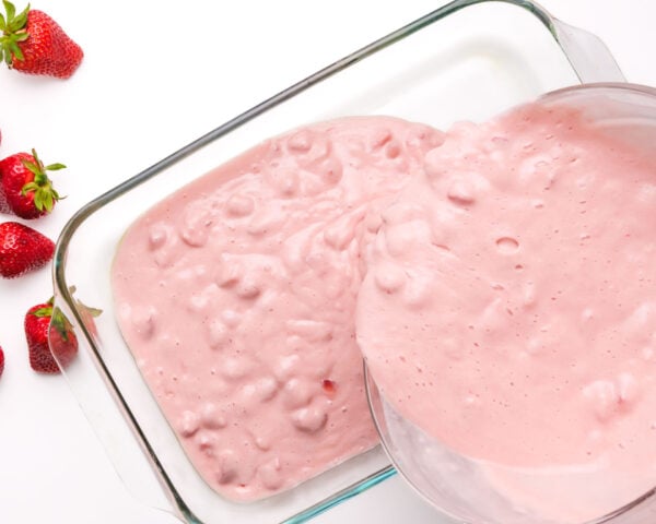 Pink cake batter is being poured into a 9x13 baking dish.