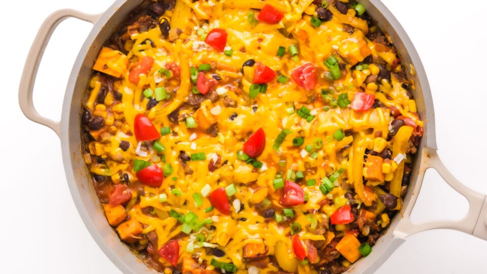 Looking down into a skillet with a taco mixture topped with melted cheese and other taco toppings.