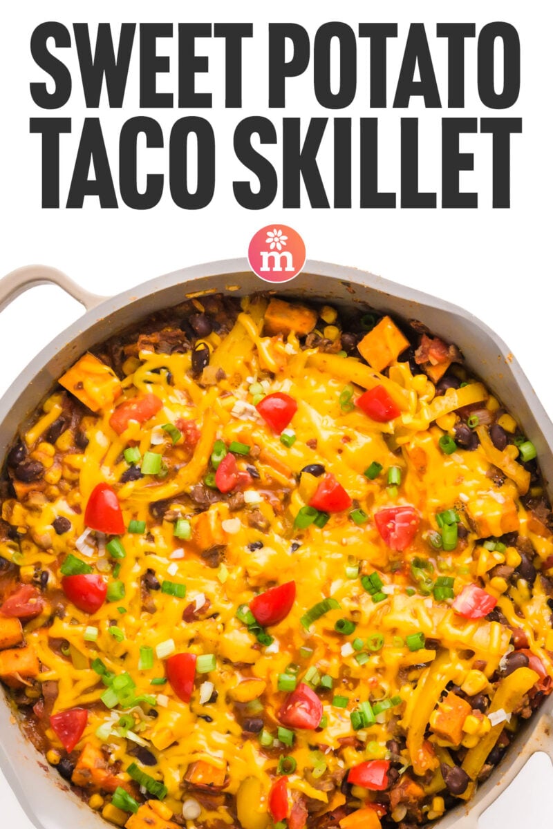 A skillet filled with sweet potato, black beans, corn, tomatoes, and melted cheese, topped with green onions.