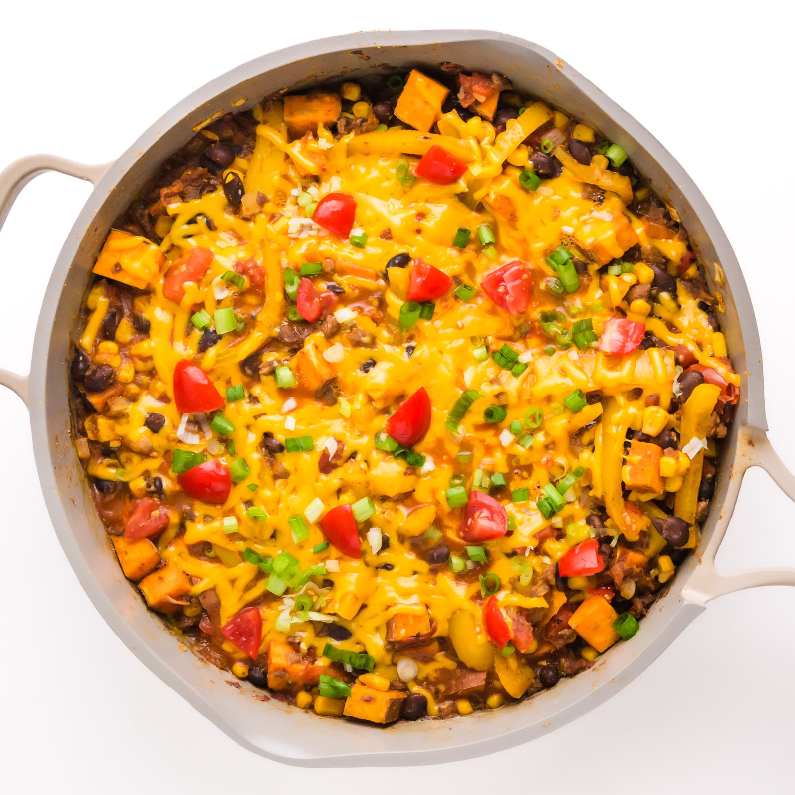 Looking into a pan full of sweet potato taco skillet with melted cheese and taco toppings on top.