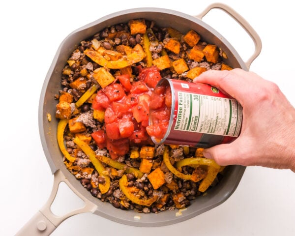 Tomatoes are being poured into a skillet with taco fixings.