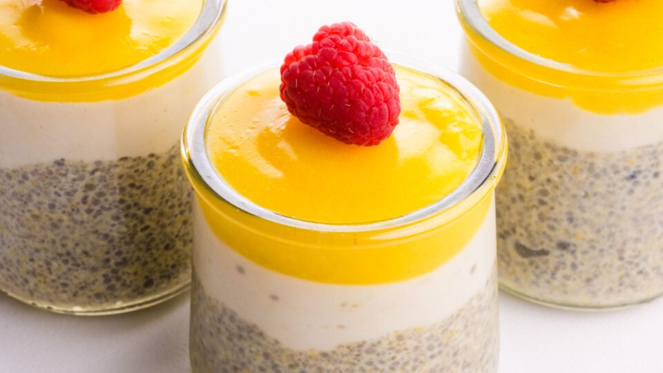 A closeup of lemon chia pudding in a glass serving jars with a raspberry on top.