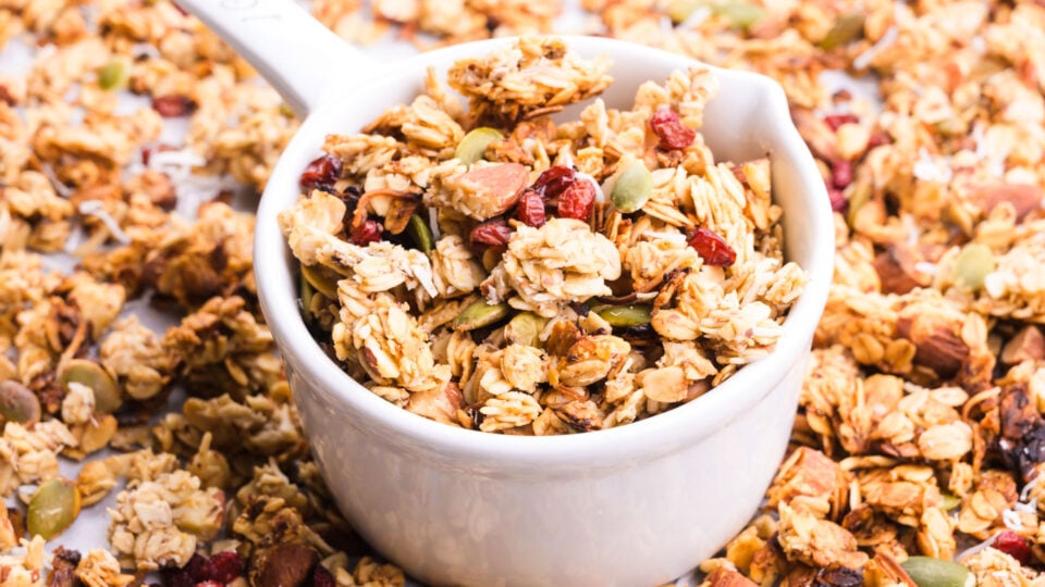 A white container holds granola on a pan with more granola beside it.