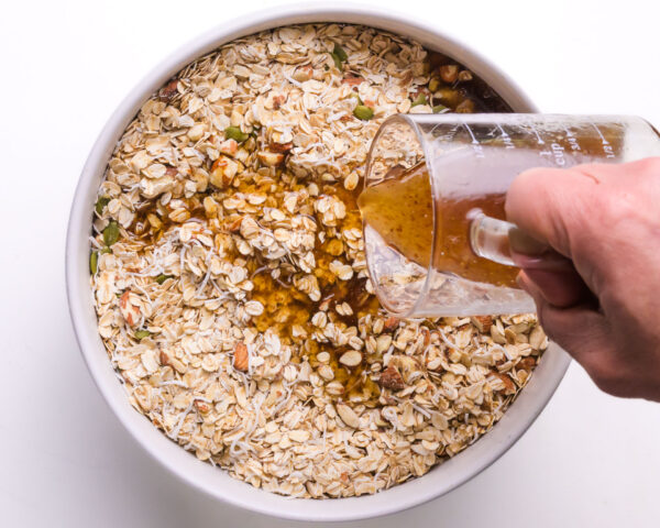 A syrup mixture is being poured over oats mixutre in a large bowl.