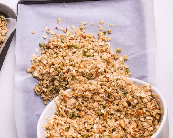 Sticky granola mixture is being poured into a pan lined with parchment paper.