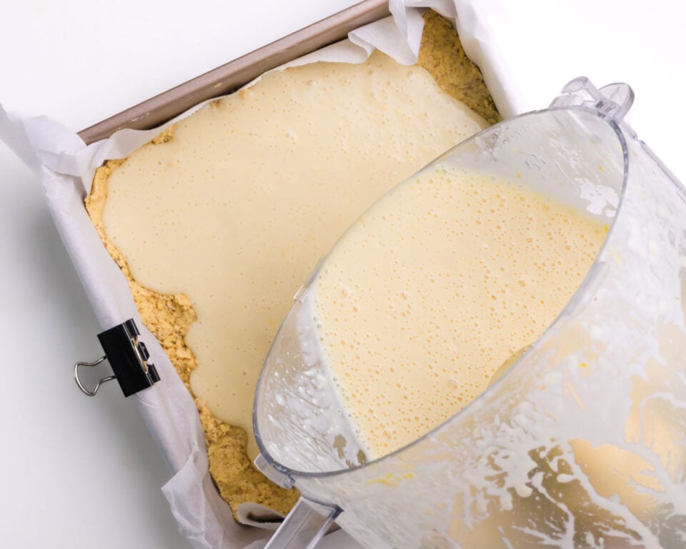 A creamy filling is being poured over a crust in a pan.