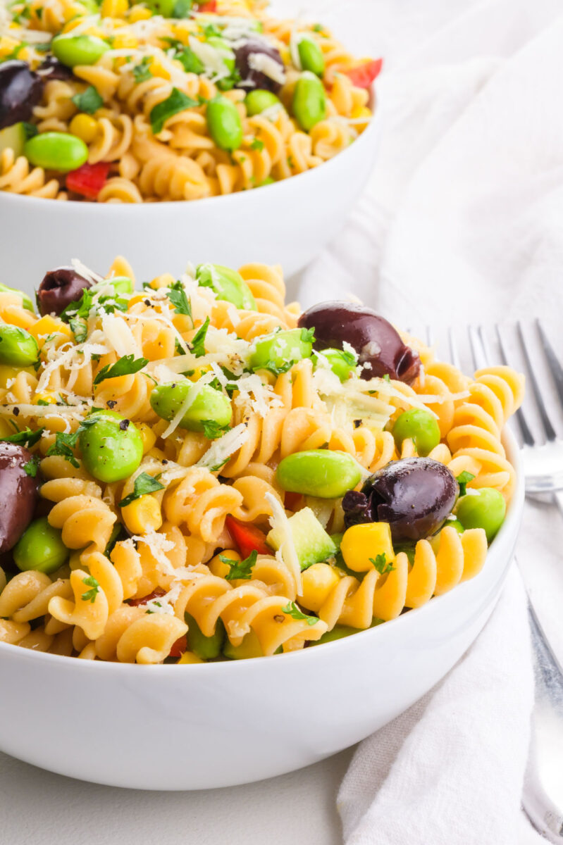 Two bowls are full of pasta salad with kalamata olives and edamame on top.