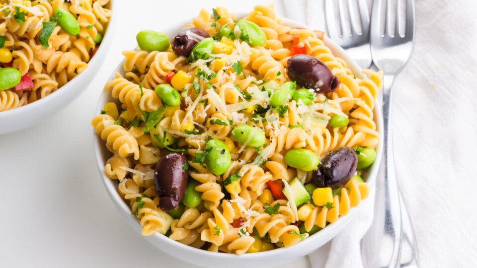 Two bowls are full of pasta salad with colorful toppings sitting next to forks.