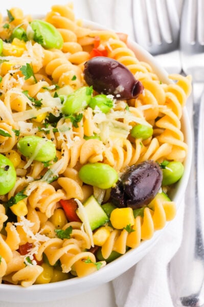 A bowl of pasta salad has edamame and olives on top.