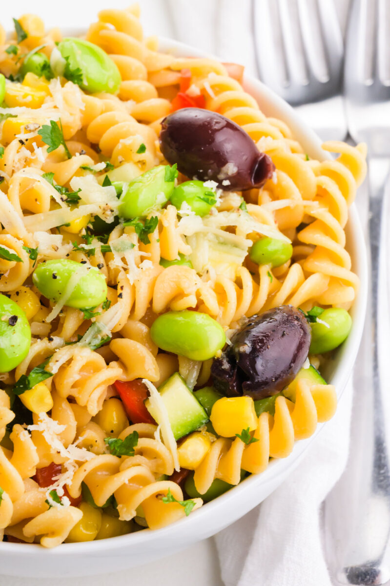 A bowl of pasta salad has edamame and olives on top.