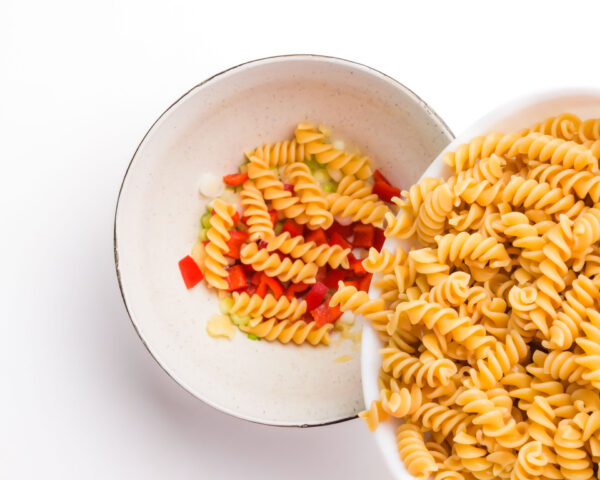 Pasta is being poured into a bowl with veggies in it.