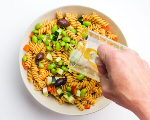 Dressing is being poured over pasta salad with colorful veggies.