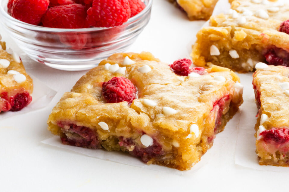 Slices of raspberry white chocolate blondies next to a bowl of fresh raspberries.