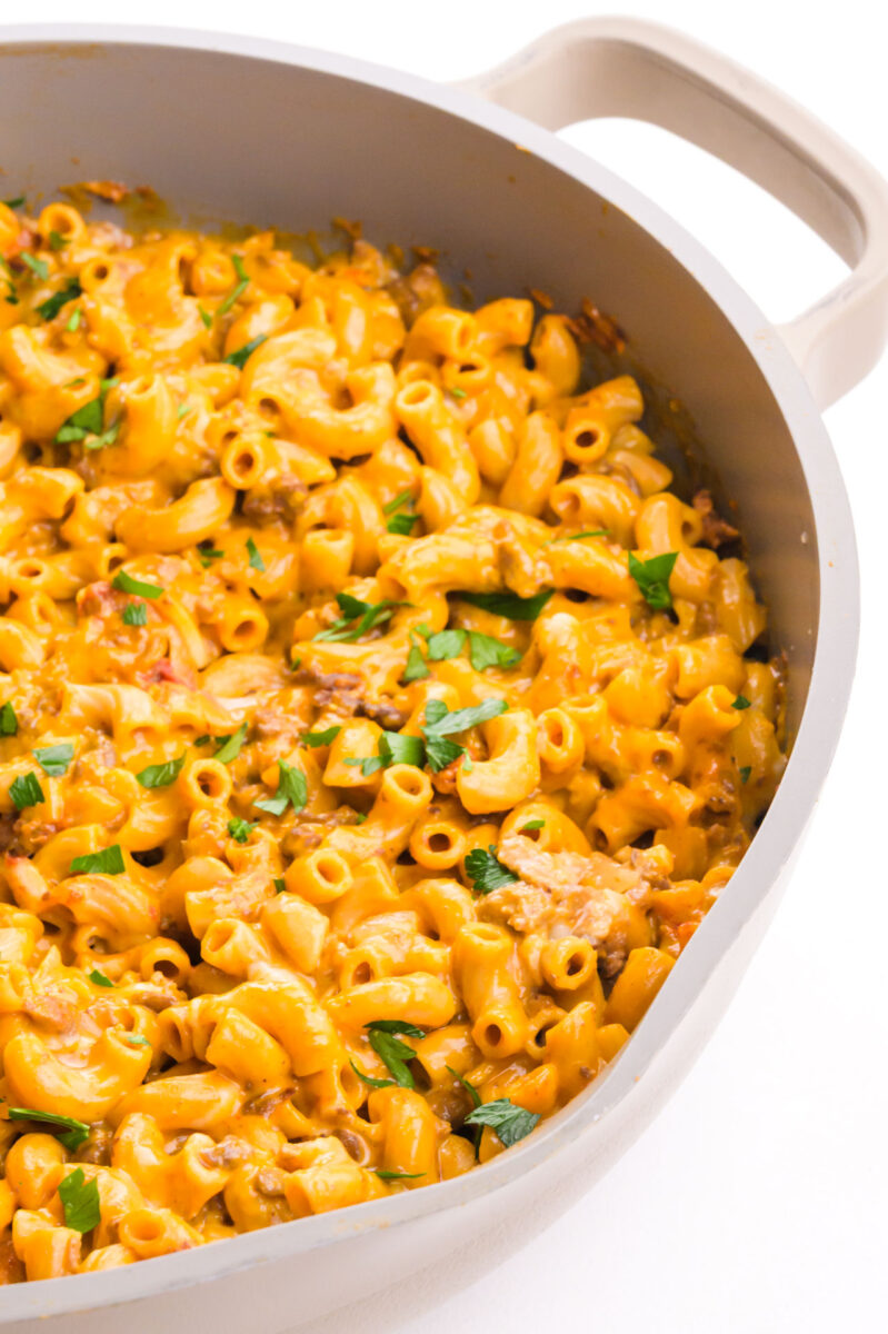 Creamy one-pot vegan cheesy hamburger helper in a skillet topped with fresh chopped parsley.