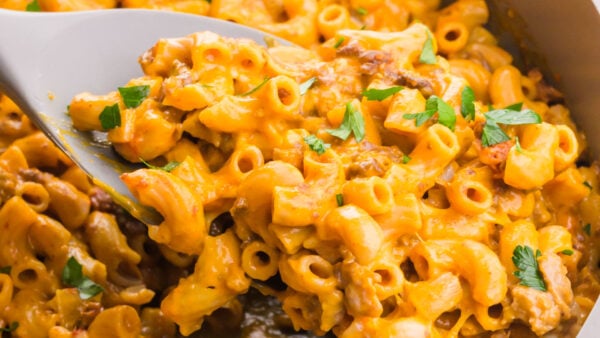 Creamy macaroni is being spooned out of a skillet.