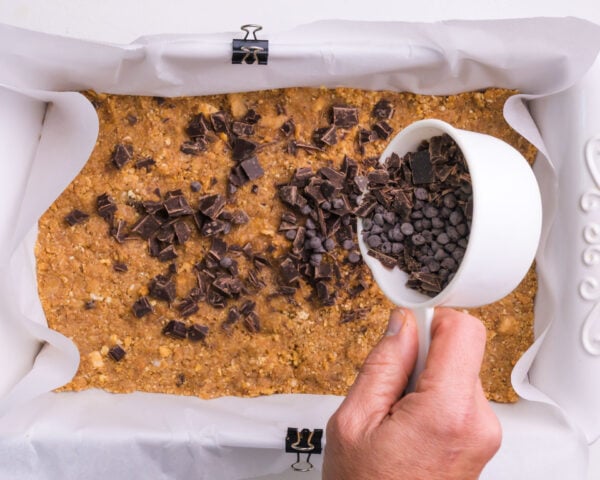 Chocolate chips are being spread over a crust in a baking dish.