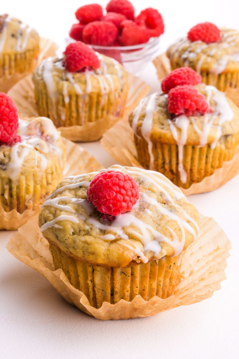 Several muffins on a table with raspberries on top of each.