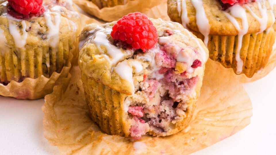 Several raspberry muffins on a table, one with a bite taken out.