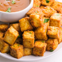 A closeup of crispy fried tofu near a bowl of sauce.