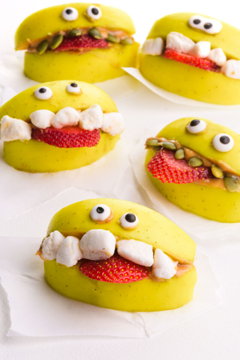 Several apple monster treats are on a table, with candy eyes and marshmallows for teeth.