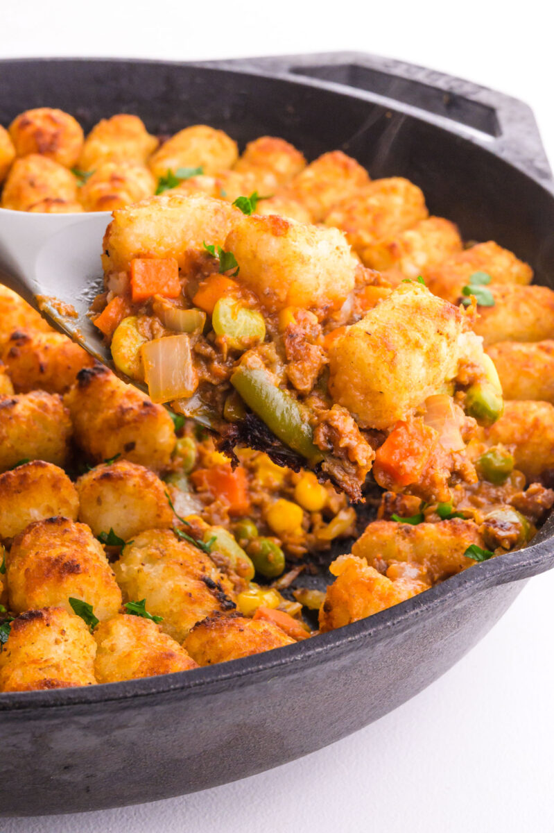 A serving of beyond beef shepherd's pie hovers over a skillet with the rest of the dish.
