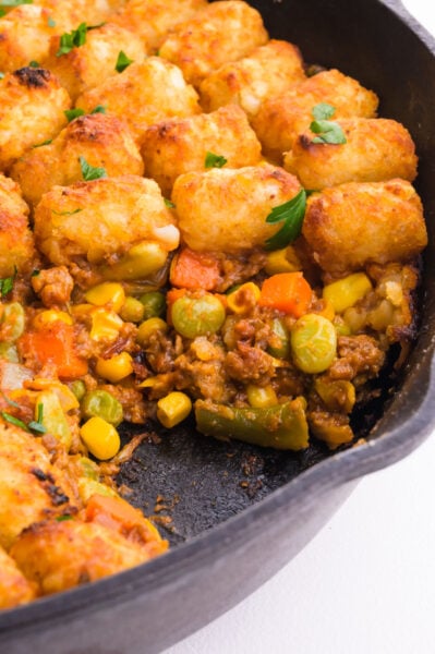 A skillet with shepherd's pie with tater tots shows a bite taken out revealing the filling.
