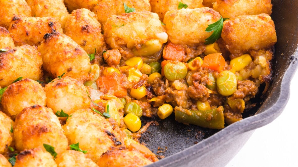 A cast iron skillet holds shepherd's pie with tater tots on top.