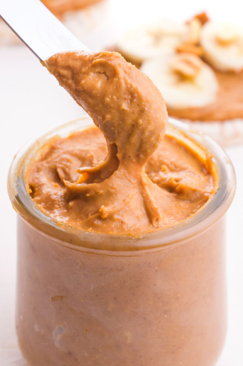 A knife takes a scoop of peanut butter from a jar.