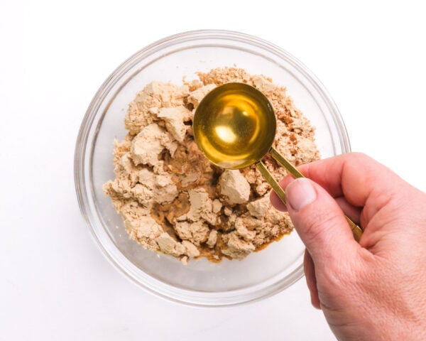 Olive oil is being poured into a bowl with peanut butter powder.