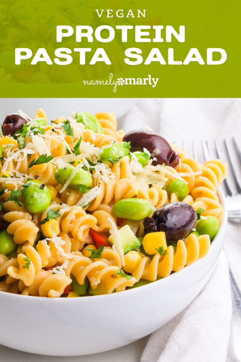 Vegan protein pasta salad with colorful vegetables, topped with herbs and olives in a white bowl.