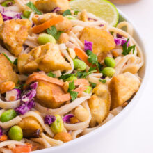 A bowl of thai noodle salad is topped with fried tofu and other inredients.