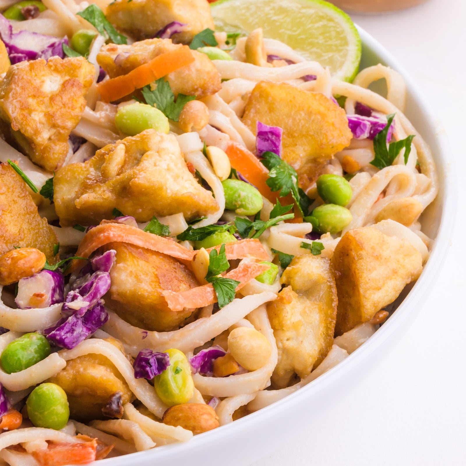 A bowl of thai noodle salad is topped with fried tofu and other inredients.