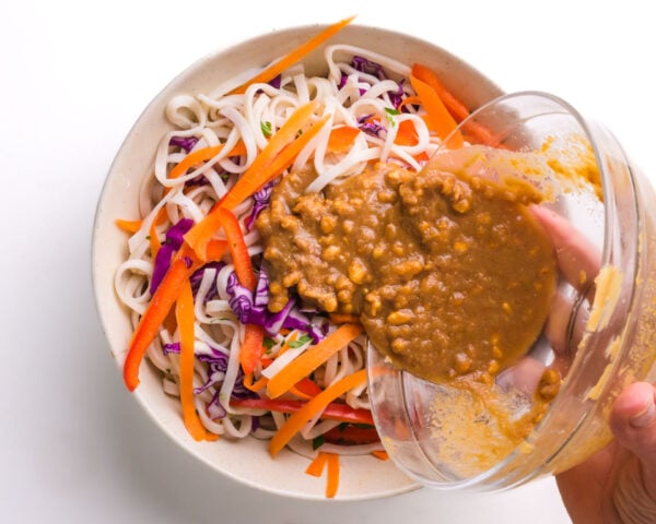 Peanut sauce is being poured over noodles and other ingredients.