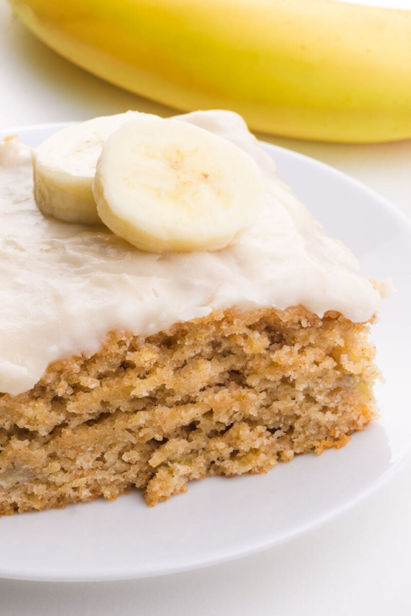 A closeup of banana snacking cake on a plate with a banana behind it.
