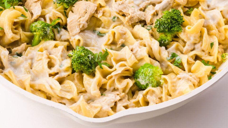 Looking down on a white skillet with vegan chicken Alfredo noodles and broccoli.