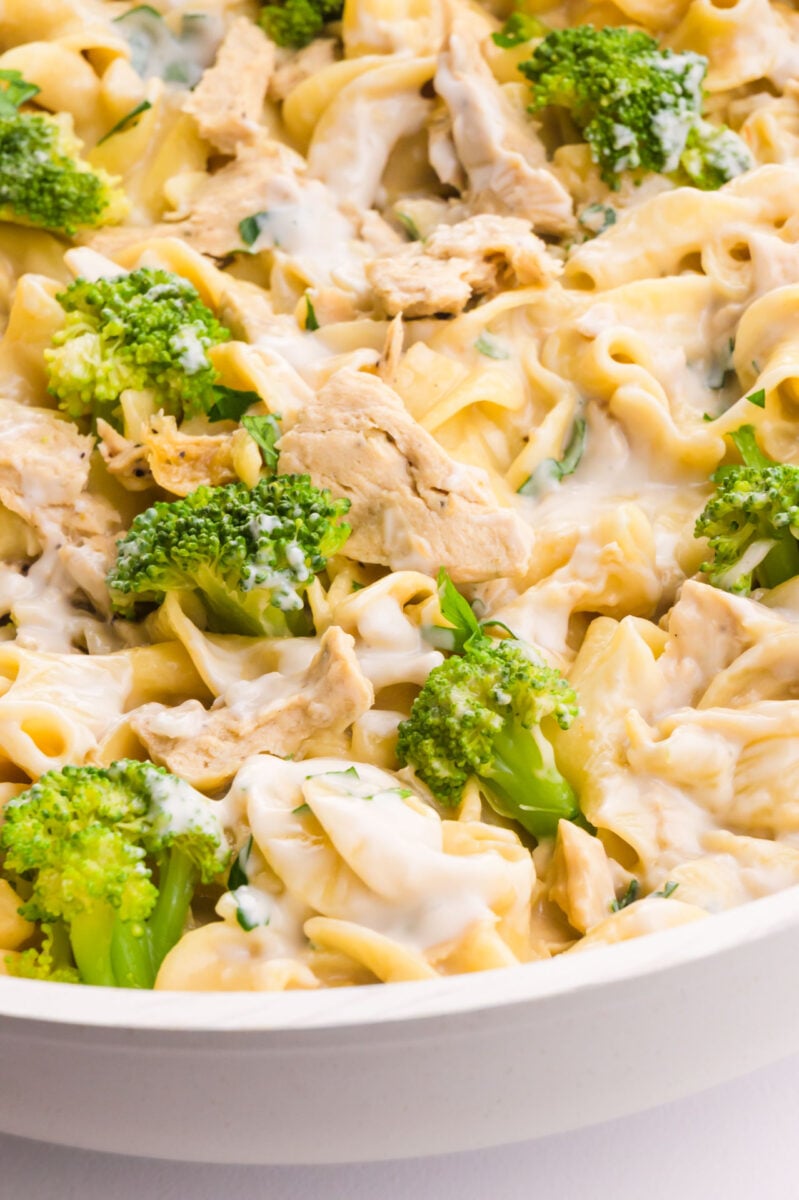 Vegan chicken Alfredo is in a white skillet with broccoli pieces.