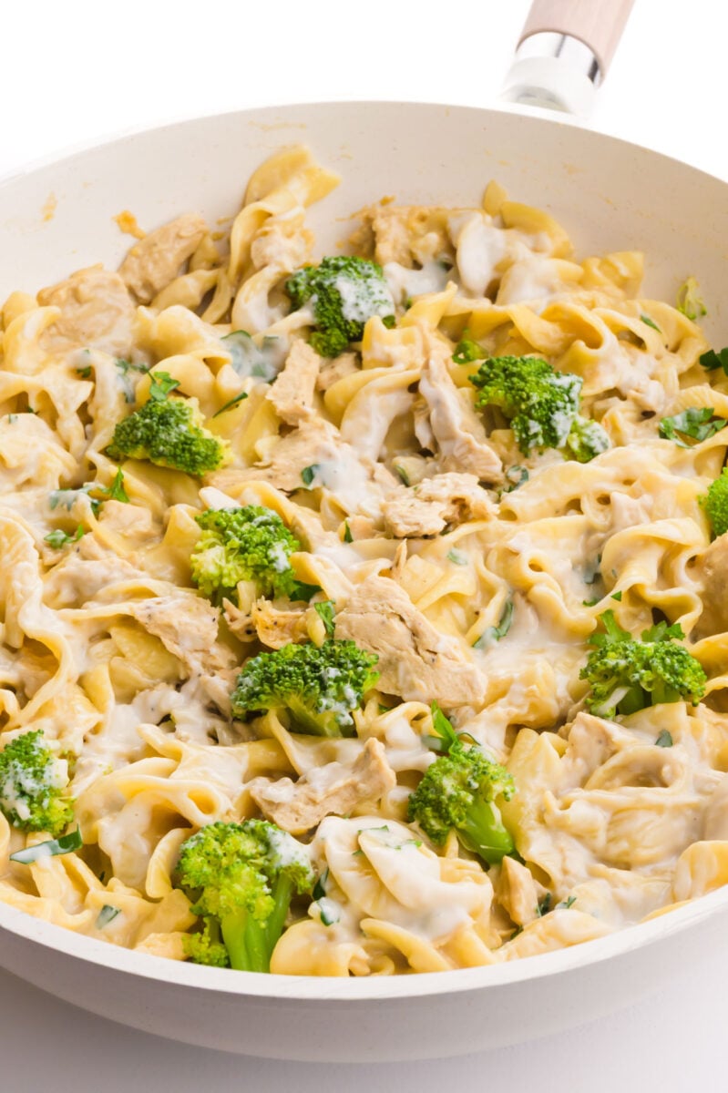 A white skillet holds vegan chicken Alfredo along with broccoli florets.