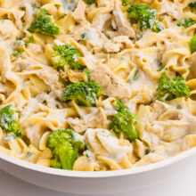 Creamy pasta with chicken and broccoli, garnished with fresh herbs in a serving dish.