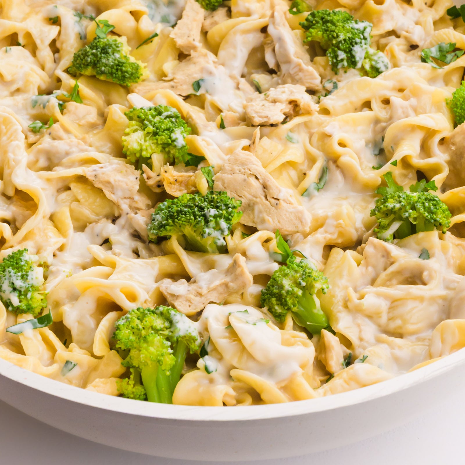 Creamy pasta with chicken and broccoli, garnished with fresh herbs in a serving dish.